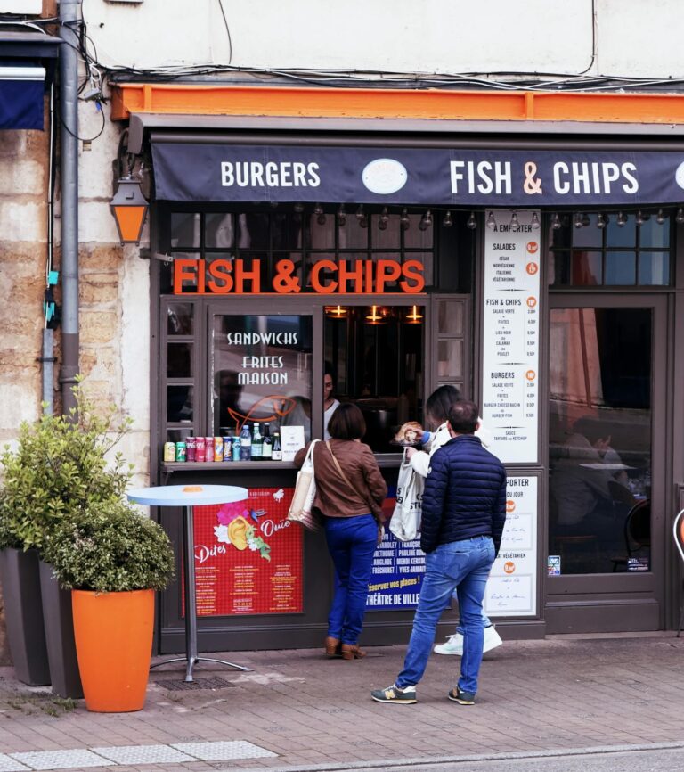Outdoor view of a French fish & chips eatery with customers engaged at the order counter.