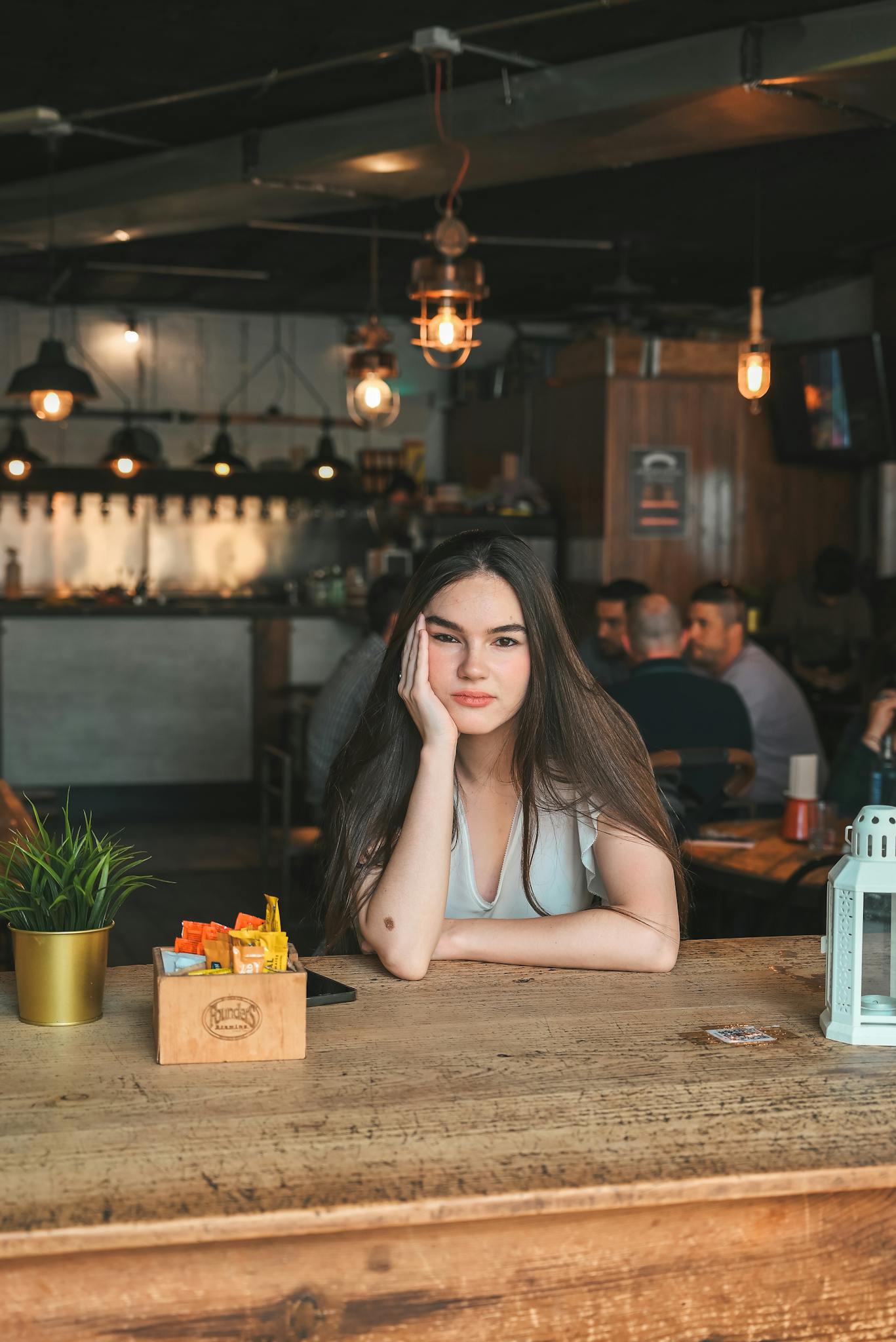 Young woman sits casually in a warm, rustic restaurant environment. Modern interior, inviting atmosphere.